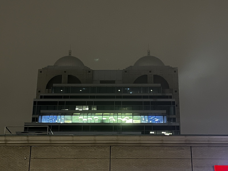 Nighttime photo of the building. One floor is lit up with blue and green lights.
