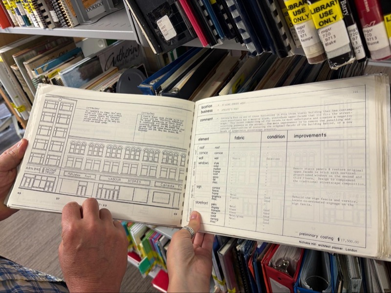 Open book held by a pair of hands, showing architectural facade sketches