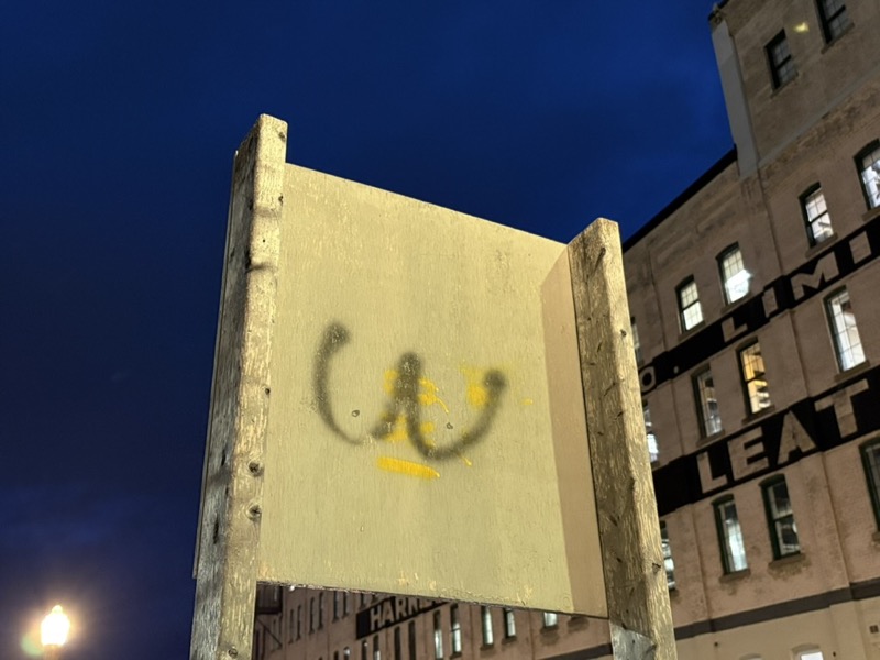 Back of a construction sign, upon which has been spray-painted minimalist breasts... or a letter W