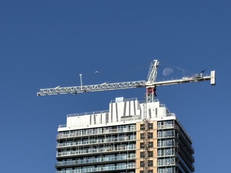 Crane atop TEK Tower, with moon in a clear blue sky